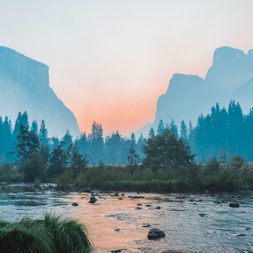 Distant mountains serve as a hazy backdrop to a tranquil river and everygreen forest.